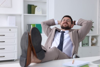 Smiling businessman with hands behind his head holding legs on table in office. Break time