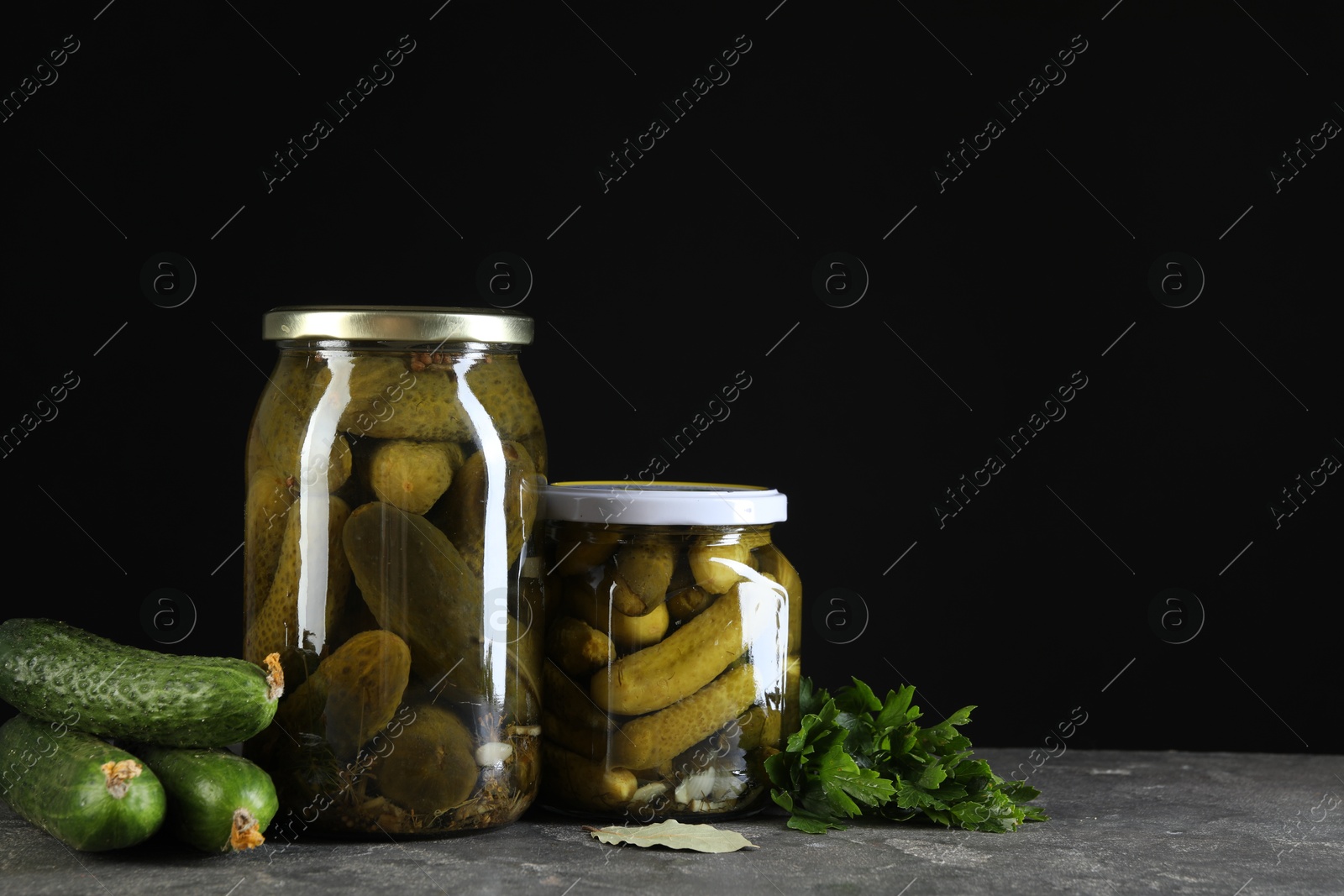 Photo of Tasty pickled cucumbers in jars and fresh ingredients on grey textured table, space for text