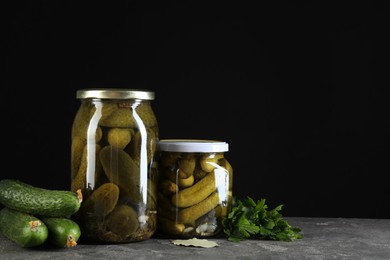 Photo of Tasty pickled cucumbers in jars and fresh ingredients on grey textured table, space for text