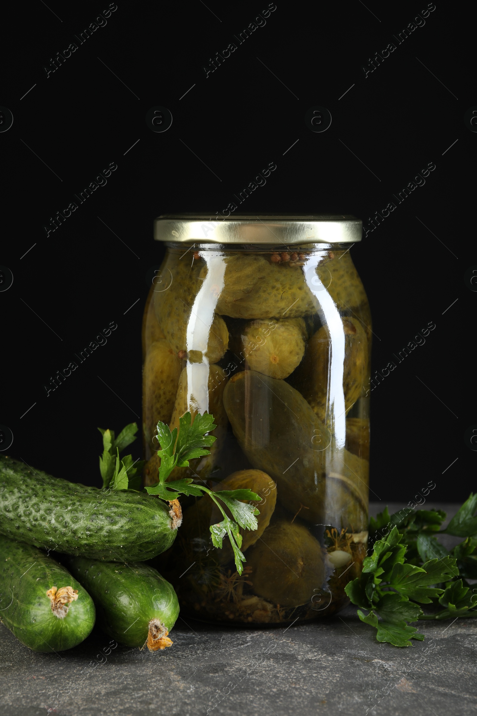 Photo of Tasty pickled cucumbers in jar and fresh ingredients on grey textured table