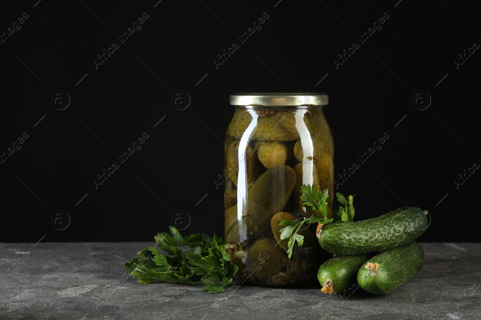 Photo of Tasty pickled cucumbers in jar and fresh ingredients on grey textured table, space for text