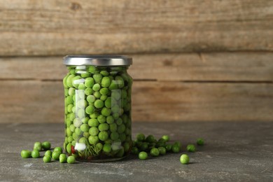 Photo of Tasty pickled green peas in jar on grey textured table, space for text