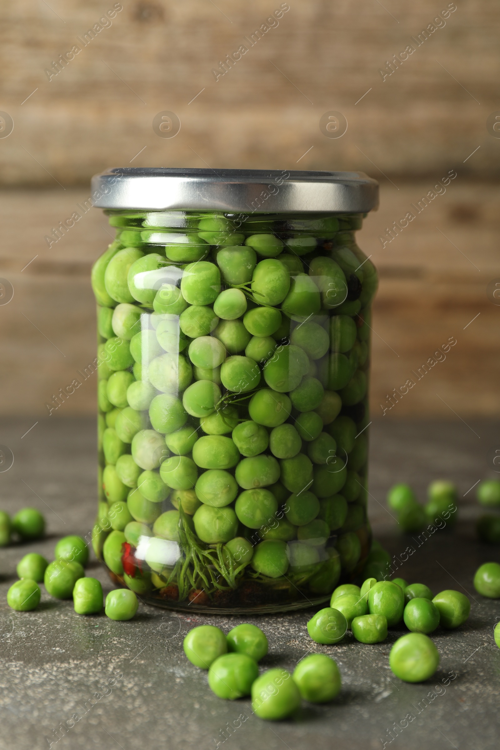 Photo of Tasty pickled green peas in jar on grey textured table, closeup