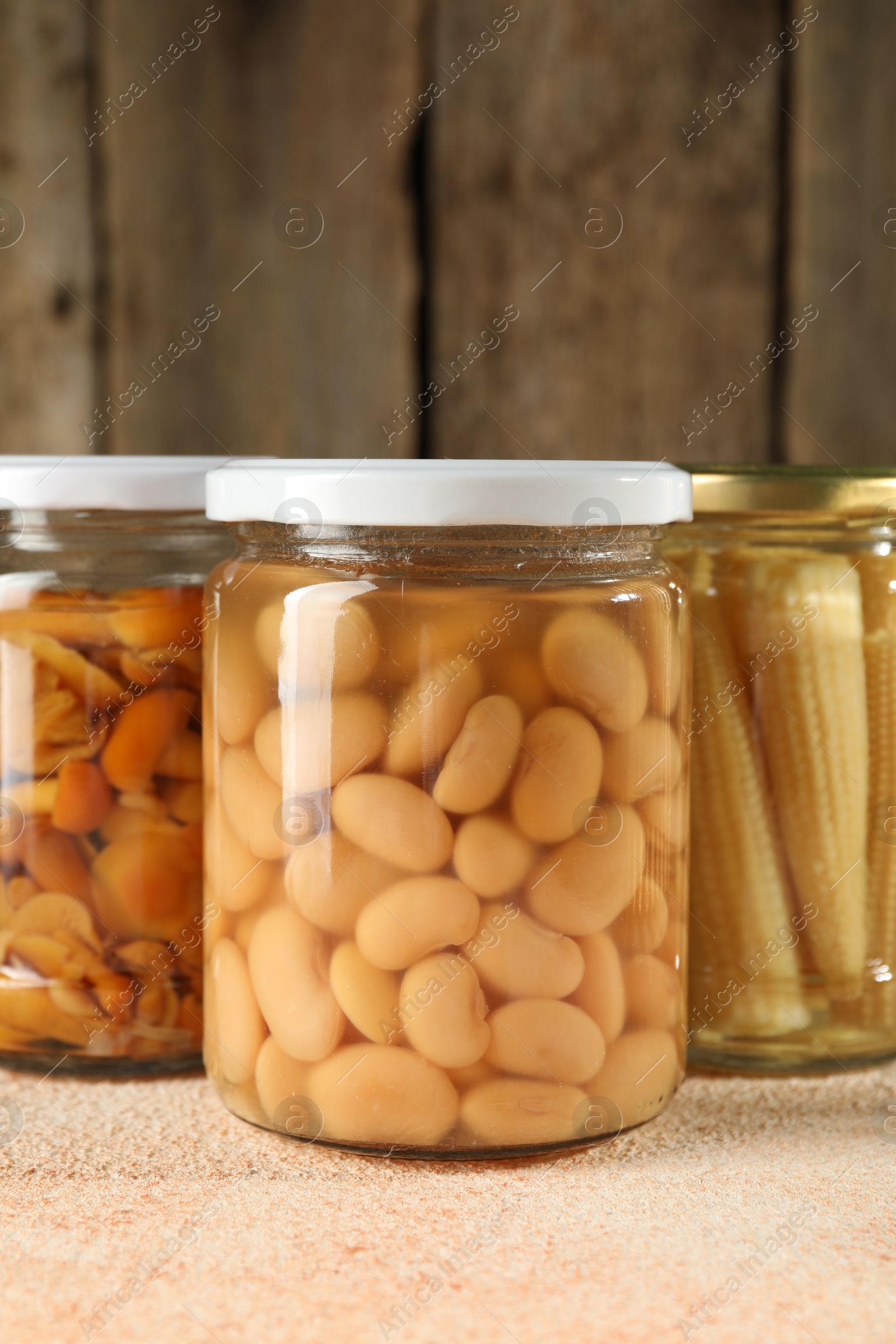 Photo of Different pickled products in jars on beige textured table, closeup