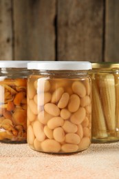 Photo of Different pickled products in jars on beige textured table, closeup