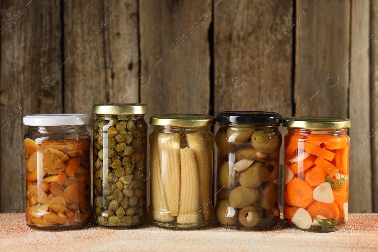 Photo of Different pickled products in jars on beige textured table