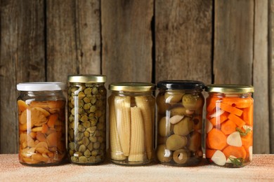 Photo of Different pickled products in jars on beige textured table