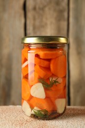 Photo of Tasty pickled vegetables in jar on beige textured table, closeup