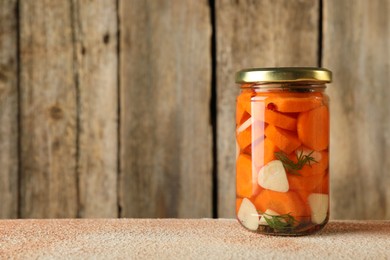 Photo of Tasty pickled vegetables in jar on beige textured table, space for text