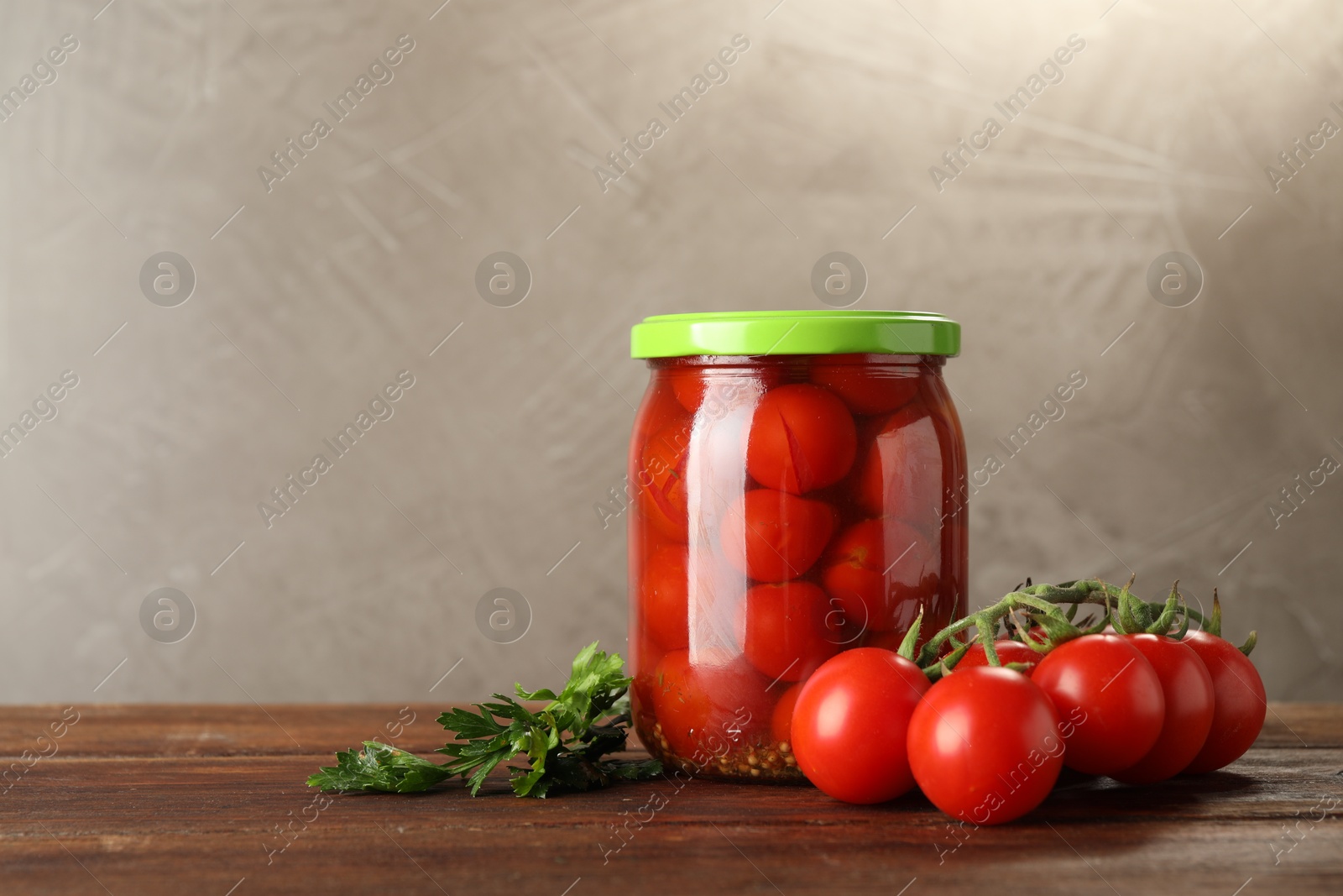 Photo of Tasty pickled tomatoes in jar and fresh ingredients on wooden table, space for text