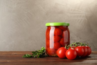 Photo of Tasty pickled tomatoes in jar and fresh ingredients on wooden table, space for text