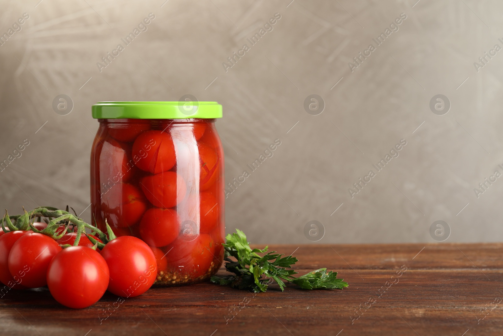 Photo of Tasty pickled tomatoes in jar and fresh ingredients on wooden table, space for text