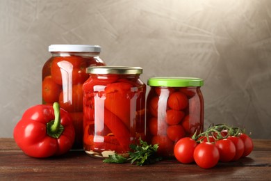 Photo of Different pickled vegetables in jars and fresh ingredients on wooden table