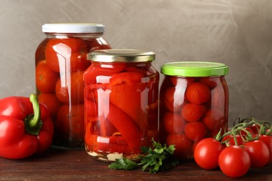 Photo of Different pickled vegetables in jars and fresh ingredients on wooden table