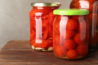 Photo of Different pickled vegetables in jars on wooden table, closeup