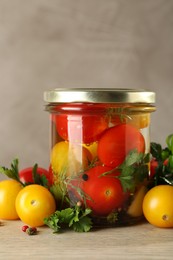 Photo of Different pickled tomatoes in jar and fresh ingredients on wooden table, closeup