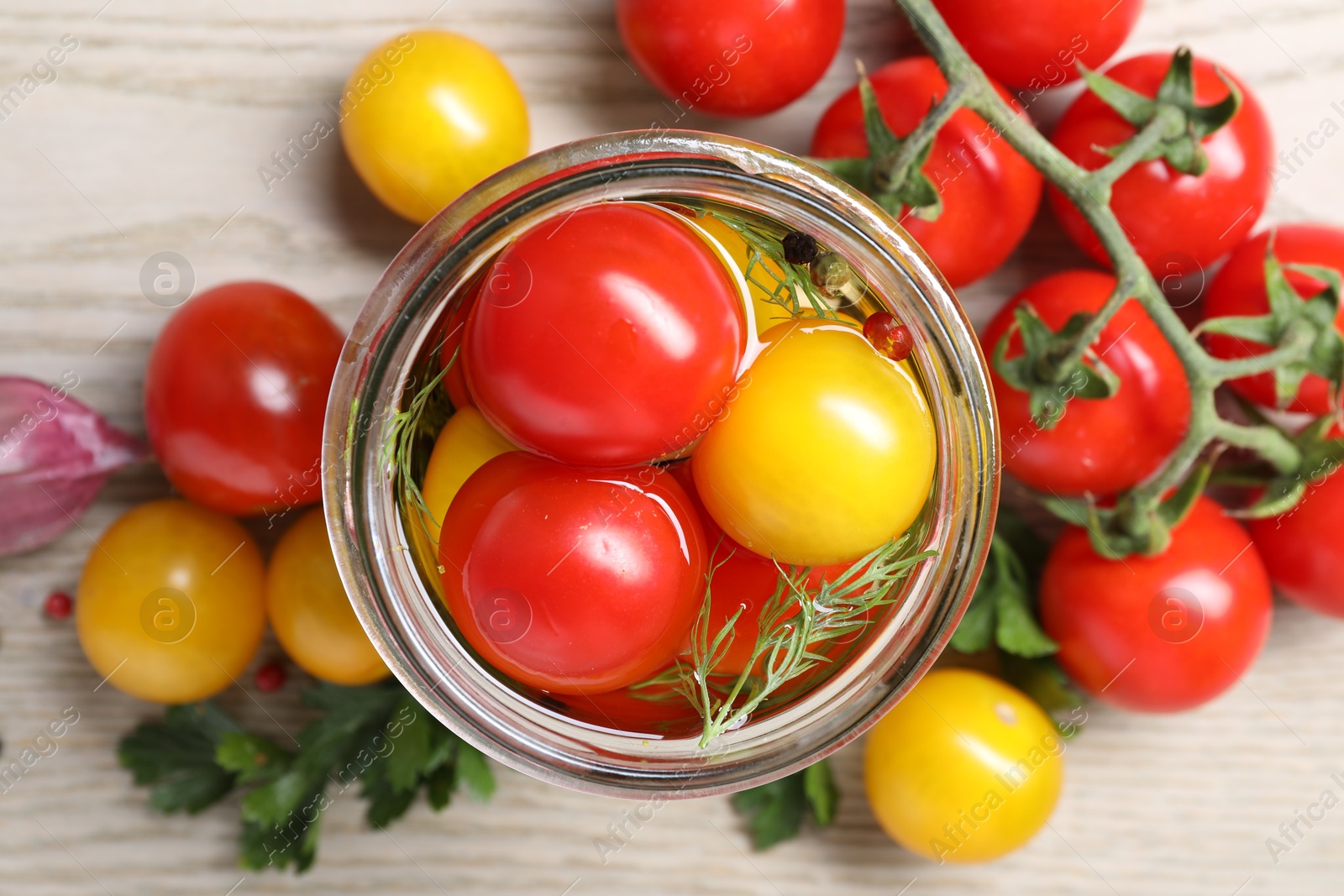 Photo of Different pickled tomatoes in jar on wooden table, flat lay