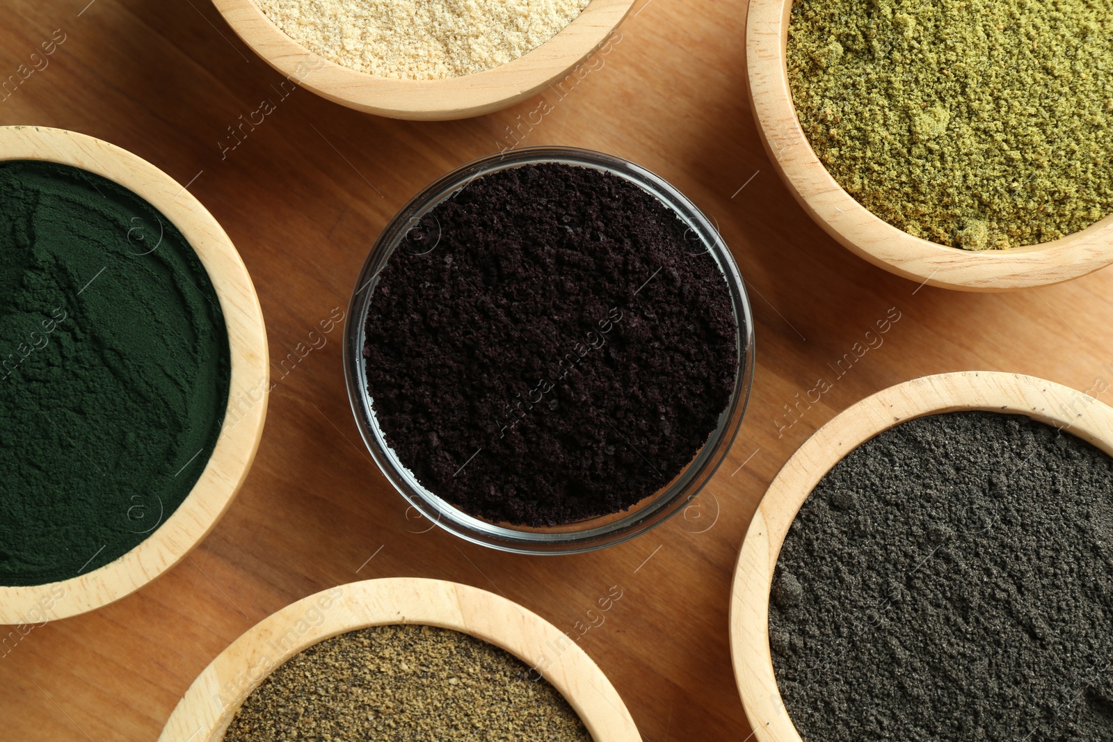 Photo of Different superfood powders in bowls on wooden table, flat lay