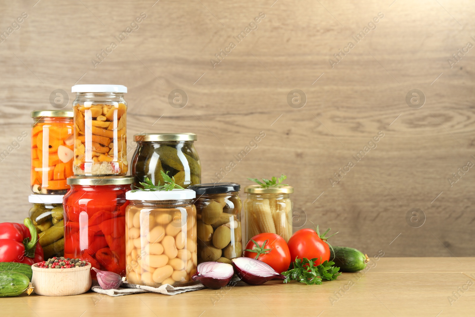 Photo of Different pickled products in jars and fresh ingredients on wooden table, space for text