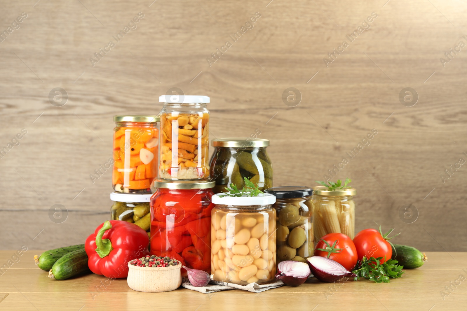 Photo of Different pickled products in jars and fresh ingredients on wooden table