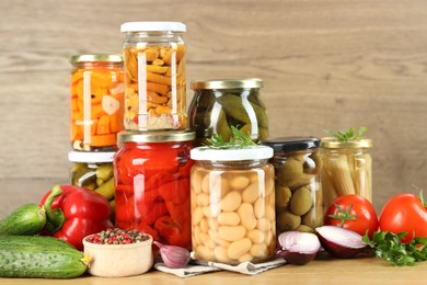 Photo of Different pickled products in jars and fresh ingredients on wooden table