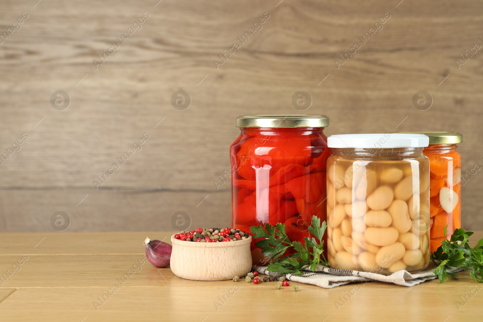 Photo of Different pickled products in jars and spices on wooden table, space for text