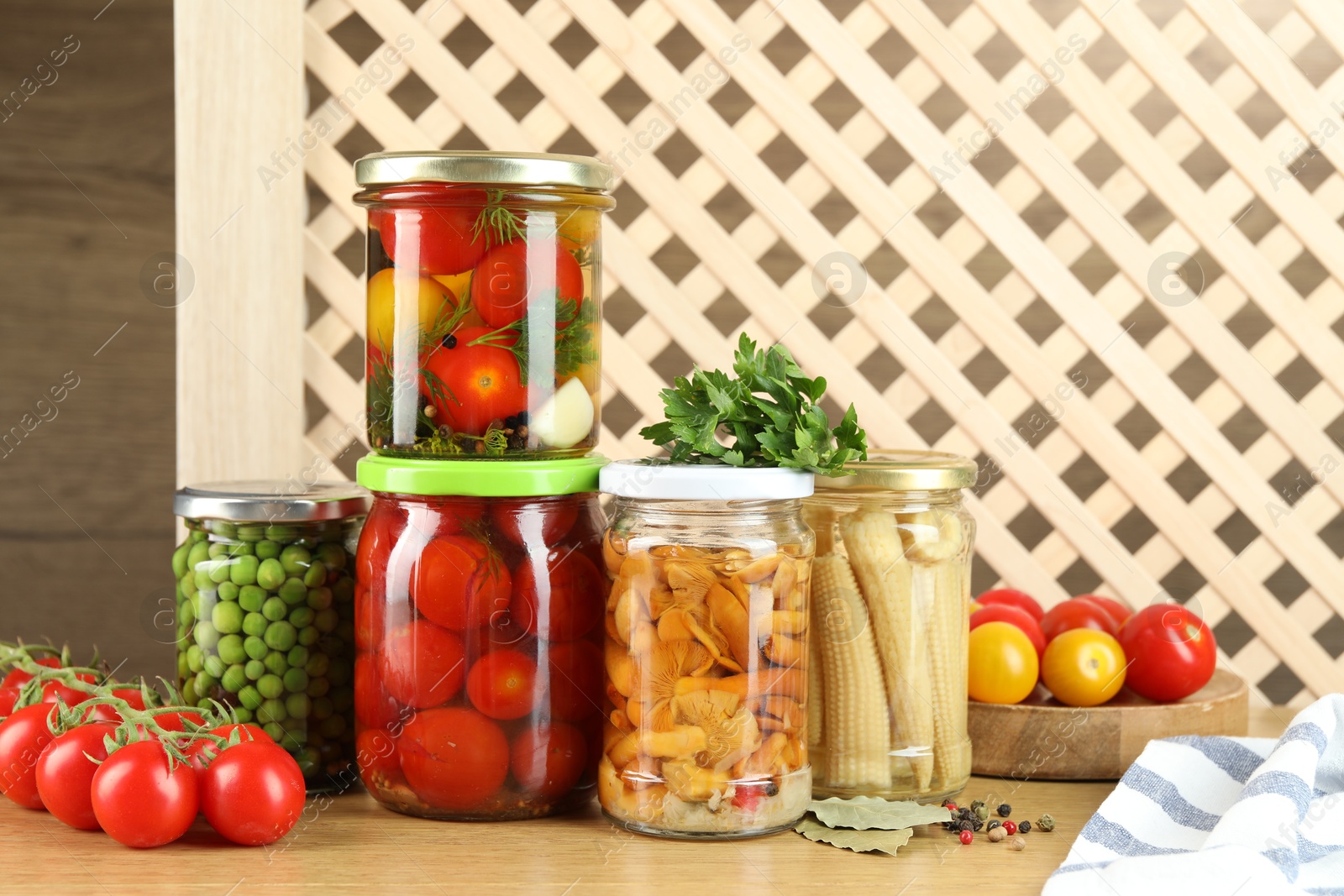 Photo of Different pickled products in jars, fresh tomatoes and spices on wooden table