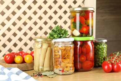 Photo of Different pickled products in jars, fresh tomatoes and spices on wooden table