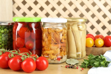 Photo of Different pickled products in jars, fresh tomatoes and spices on wooden table