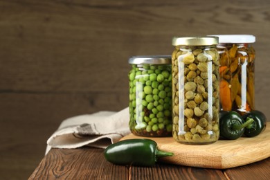 Photo of Different pickled products in jars and fresh jalapeno peppers on wooden table