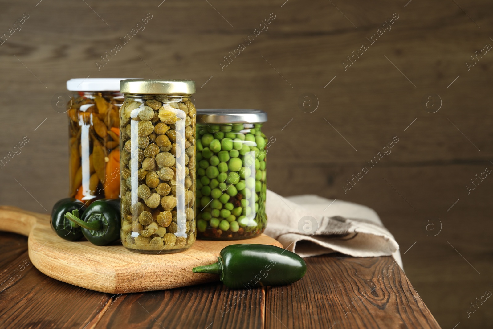 Photo of Different pickled products in jars and fresh jalapeno peppers on wooden table