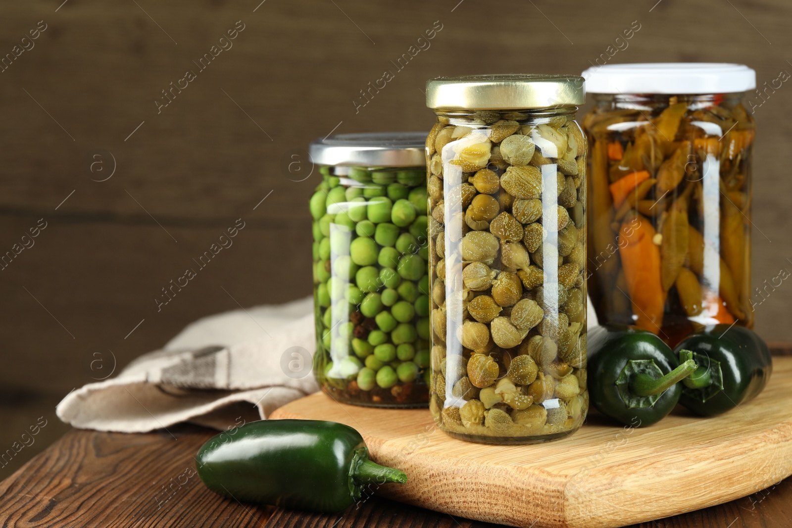 Photo of Different pickled products in jars and fresh jalapeno peppers on wooden table