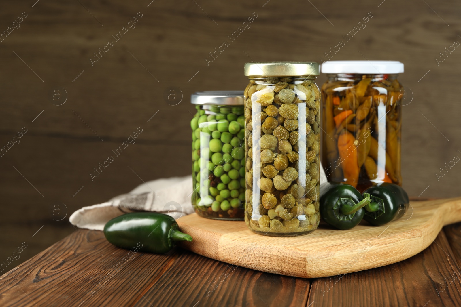 Photo of Different pickled products in jars and fresh jalapeno peppers on wooden table