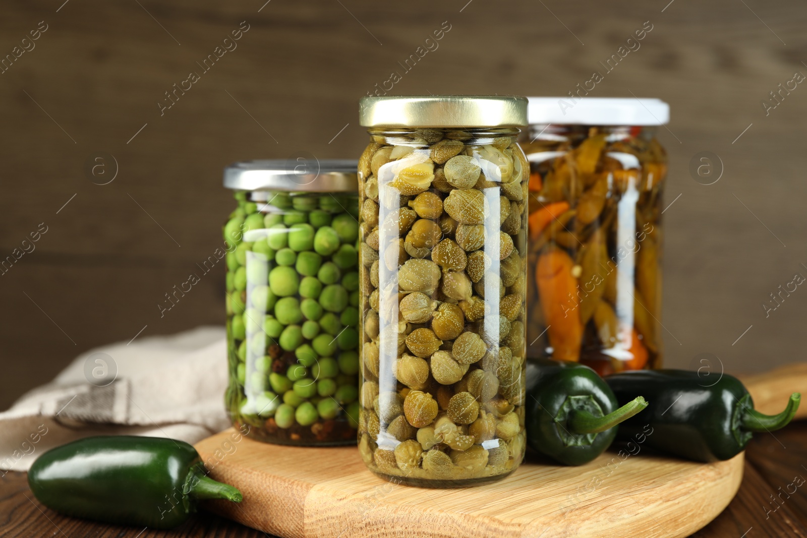 Photo of Different pickled products in jars and fresh jalapeno peppers on wooden table