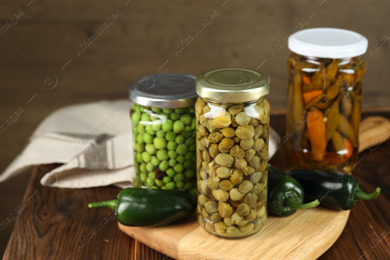 Photo of Different pickled products in jars and fresh jalapeno peppers on wooden table