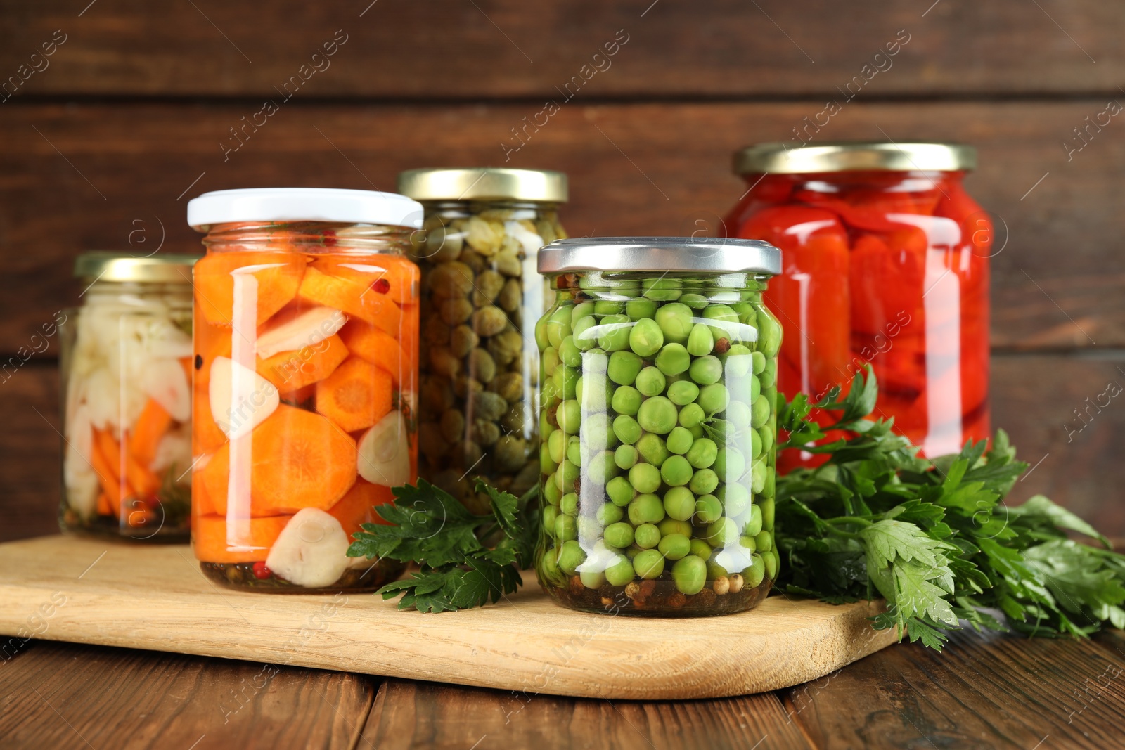 Photo of Different pickled products in jars and fresh parsley on wooden table