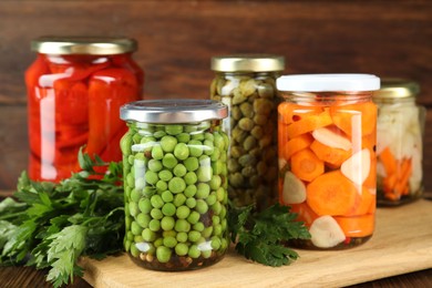 Photo of Different pickled products in jars and fresh parsley on wooden table