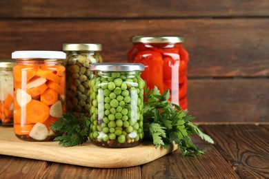 Photo of Different pickled products in jars and fresh parsley on wooden table