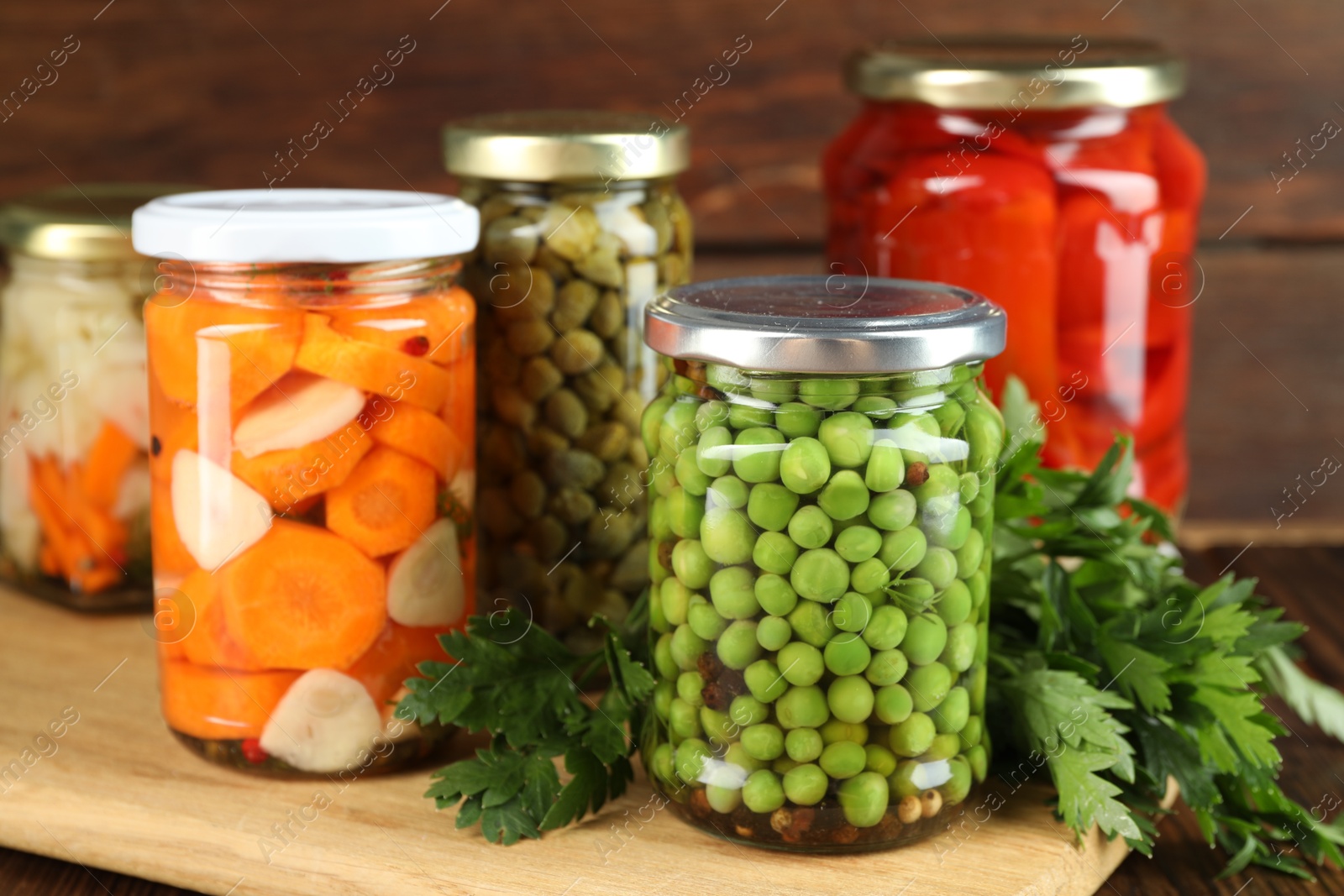 Photo of Different pickled products in jars and fresh parsley on table