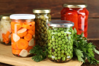 Photo of Different pickled products in jars and fresh parsley on table