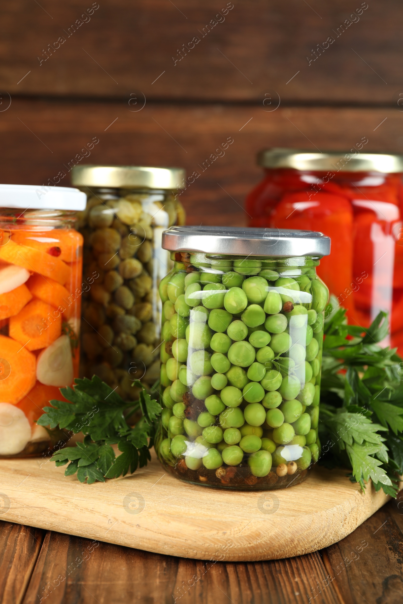 Photo of Different pickled products in jars and fresh parsley on wooden table