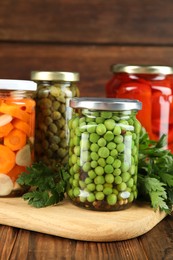 Photo of Different pickled products in jars and fresh parsley on wooden table