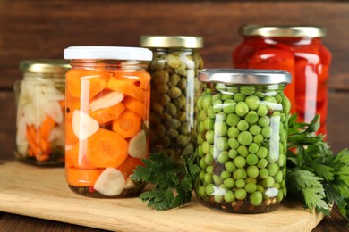 Photo of Different pickled products in jars and fresh parsley on wooden table