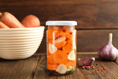 Photo of Tasty pickled carrots in jar, garlic and peppercorns on wooden table