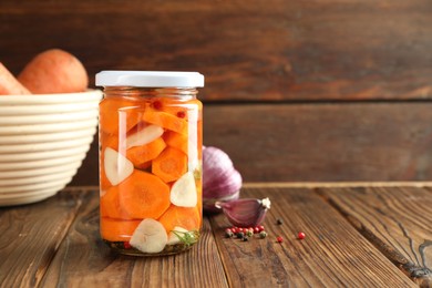 Photo of Tasty pickled carrots in jar, garlic and peppercorns on wooden table, space for text