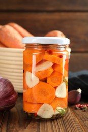 Photo of Tasty pickled carrots in jar, garlic and peppercorns on wooden table