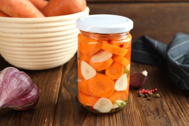 Photo of Tasty pickled carrots in jar, garlic and peppercorns on wooden table