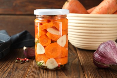 Photo of Tasty pickled carrots in jar, garlic and peppercorns on wooden table