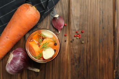 Photo of Tasty pickled carrots in jar and fresh ingredients on wooden table, flat lay. Space for text