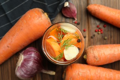 Photo of Tasty pickled carrots in jar and fresh ingredients on wooden table, flat lay